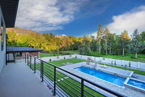 View of swimming pool featuring a balcony, a fenced backyard, a water slide, a mountain view, and a pool with connected hot tub