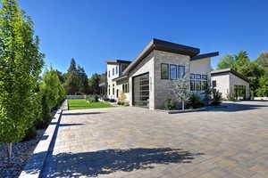 Back of house with stone siding, stucco siding, decorative driveway, and an attached garage