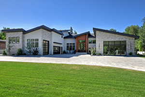 View of front of property featuring stone siding, decorative driveway, a front lawn, a garage, and stucco siding