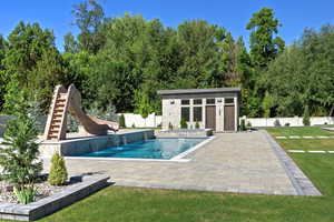 View of pool featuring a water slide, an outbuilding, a pool with connected hot tub, and a storage structure