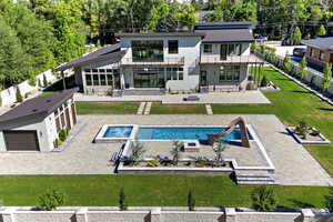 Rear view of property featuring a patio, stucco siding, stone siding, a pool with connected hot tub, and a balcony
