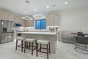 Kitchen featuring light brown cabinetry, stainless steel appliances, a kitchen bar, a center island, and recessed lighting