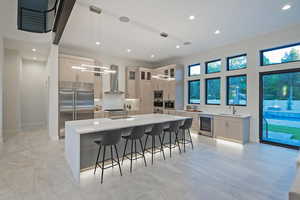 Kitchen featuring a breakfast bar area, light stone countertops, recessed lighting, built in appliances, and a large island with sink
