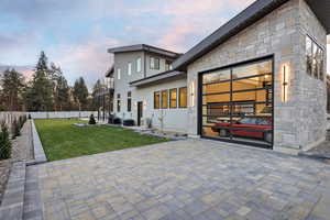 Back of house at dusk with stone siding, a fenced backyard, a garage, and a patio