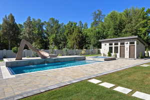 View of pool with an outbuilding, a water slide, a storage structure, a patio area, and a pool with connected hot tub