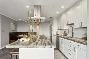 Kitchen with crown molding, decorative backsplash, a kitchen island, light stone counters, and white cabinetry