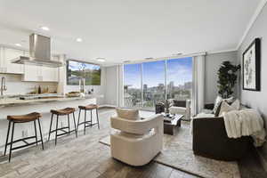 Living area with light wood-style flooring, floor to ceiling windows, crown molding, a city view, and recessed lighting