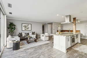 Kitchen with white cabinets, a breakfast bar, island range hood, recessed lighting, and ornamental molding