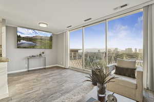 Sitting room featuring light wood finished floors, a wall of windows, ornamental molding, and a city view