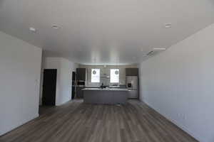 Kitchen with open floor plan, a kitchen island with sink, stainless steel fridge with ice dispenser, dark wood finished floors, and light countertops