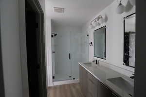 Bathroom with a shower stall, double vanity, and light wood-style flooring