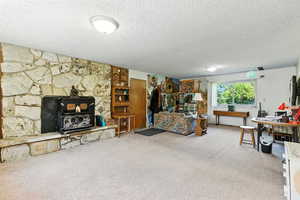 Carpeted living room with a wood stove and a textured ceiling