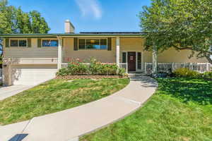 View of front of home with a porch, brick siding, an attached garage, a chimney, and driveway