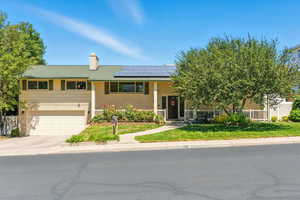 View of front of home featuring a porch, roof mounted solar panels, driveway, brick siding, and a garage