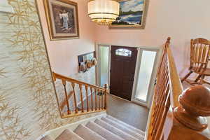 Entryway featuring stairway, light carpet, and a chandelier