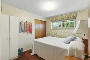 Bedroom with dark carpet, a closet, and a textured ceiling
