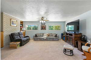 Living room featuring a textured ceiling, carpet flooring, a ceiling fan, and brick wall