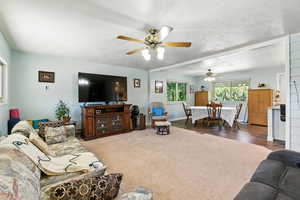 Living area featuring a textured ceiling, carpet, a ceiling fan, and beamed ceiling