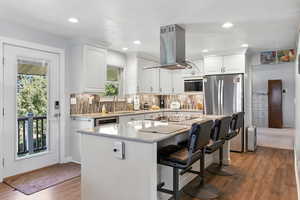 Kitchen with a breakfast bar area, dark wood-style flooring, tasteful backsplash, light stone counters, and recessed lighting
