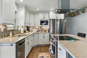 Kitchen with stainless steel appliances, light stone countertops, island range hood, white cabinetry, and recessed lighting