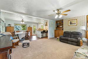 Living area with ceiling fan, a textured ceiling, carpet, and brick wall