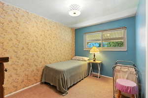 Bedroom featuring wallpapered walls, a textured ceiling, light carpet, and an accent wall