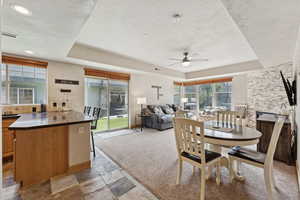 Dining room featuring a raised ceiling, stone tile floors, and a ceiling fan