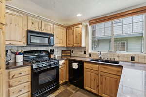 Kitchen with black appliances, decorative backsplash, light brown cabinetry, dark countertops, and recessed lighting