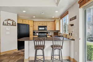 Kitchen with black appliances, decorative backsplash, light brown cabinets, a peninsula, and recessed lighting