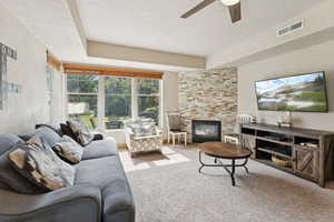 Carpeted living area with a fireplace, ceiling fan, and a raised ceiling