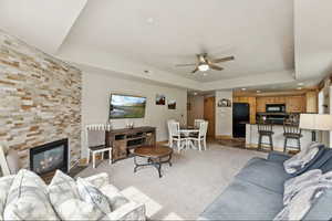 Living area featuring a raised ceiling, recessed lighting, light carpet, a fireplace, and a ceiling fan