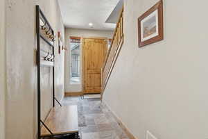 Corridor with stairway, stone finish flooring, and a textured wall