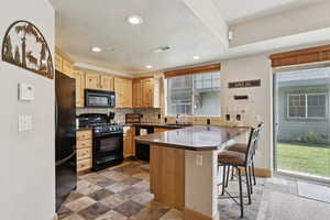 Kitchen featuring recessed lighting, backsplash, a peninsula, black appliances, and a kitchen breakfast bar
