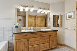 Bathroom with double vanity, a textured wall, tile patterned flooring, and a tub to relax in