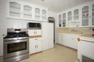 Kitchen featuring white cabinets, appliances with stainless steel finishes, glass insert cabinets, and light countertops