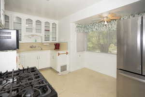 Kitchen with freestanding refrigerator, light countertops, decorative backsplash, white cabinetry, and glass insert cabinets