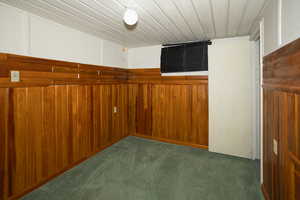 Unfurnished room featuring wood walls, dark colored carpet, and wood ceiling