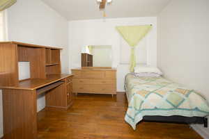 Bedroom with dark wood-style floors, a ceiling fan, and a desk