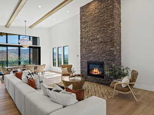 Living area featuring light wood finished floors, a chandelier, a high ceiling, a stone fireplace, and beamed ceiling