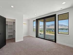 Unfurnished bedroom with a walk in closet, access to outside, recessed lighting, a water and mountain view, and light colored carpet