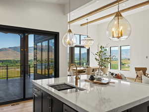 Kitchen with dark cabinetry, light stone counters, a center island with sink, hanging light fixtures, and light wood-type flooring