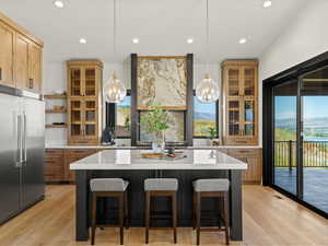 Kitchen with glass insert cabinets, recessed lighting, stainless steel built in refrigerator, light wood finished floors, and decorative light fixtures