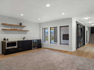 Indoor wet bar with dark cabinetry, recessed lighting, open shelves, stairs, and light wood-type flooring