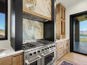 Kitchen with double oven range, decorative backsplash, light stone countertops, light wood-style flooring, and glass insert cabinets
