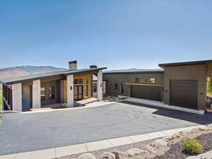 Contemporary house with a mountain view, a chimney, a garage, stone siding, and covered porch