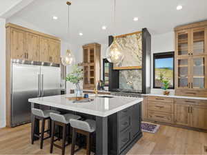 Kitchen with glass insert cabinets, built in fridge, light stone counters, decorative light fixtures, and recessed lighting