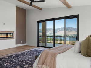 Bedroom with a water and mountain view, light wood-style floors, a glass covered fireplace, access to outside, and recessed lighting