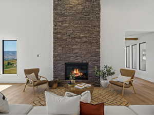 Living area with wood finished floors, a stone fireplace, and a towering ceiling