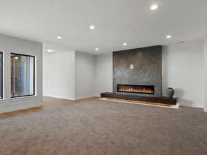 Unfurnished living room featuring recessed lighting, a large fireplace, and light colored carpet
