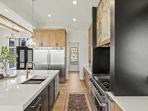 Kitchen featuring hanging light fixtures, light stone counters, lofted ceiling, premium appliances, and recessed lighting